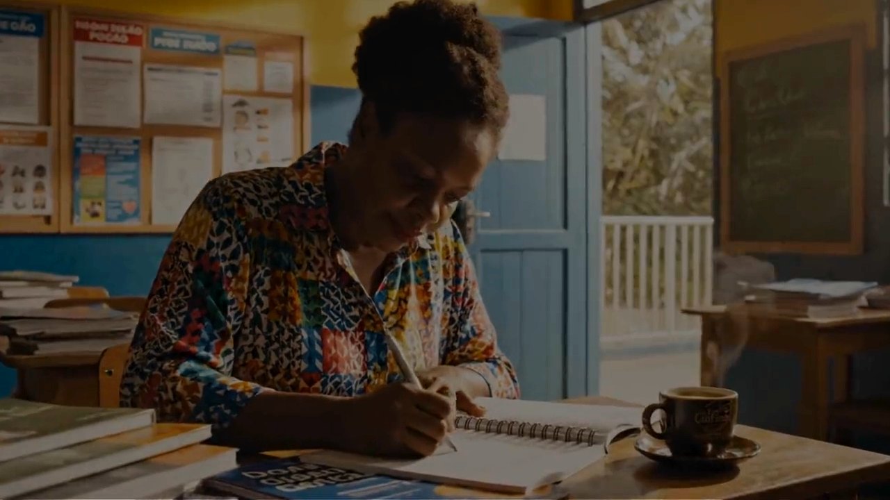 Professora escrevendo no caderno em uma sala de aula de escola pública
